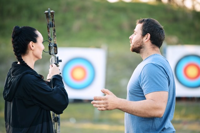 Man teaching a woman archery.