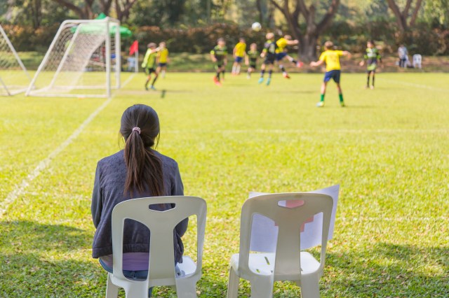 Woman watching a school boy soccer game on a sunny day