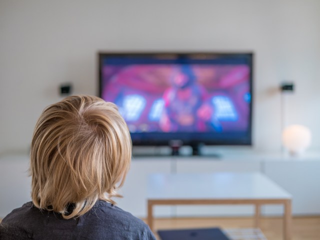 Back view image of cute little blond hair boy sitting on sofa and watching TV.